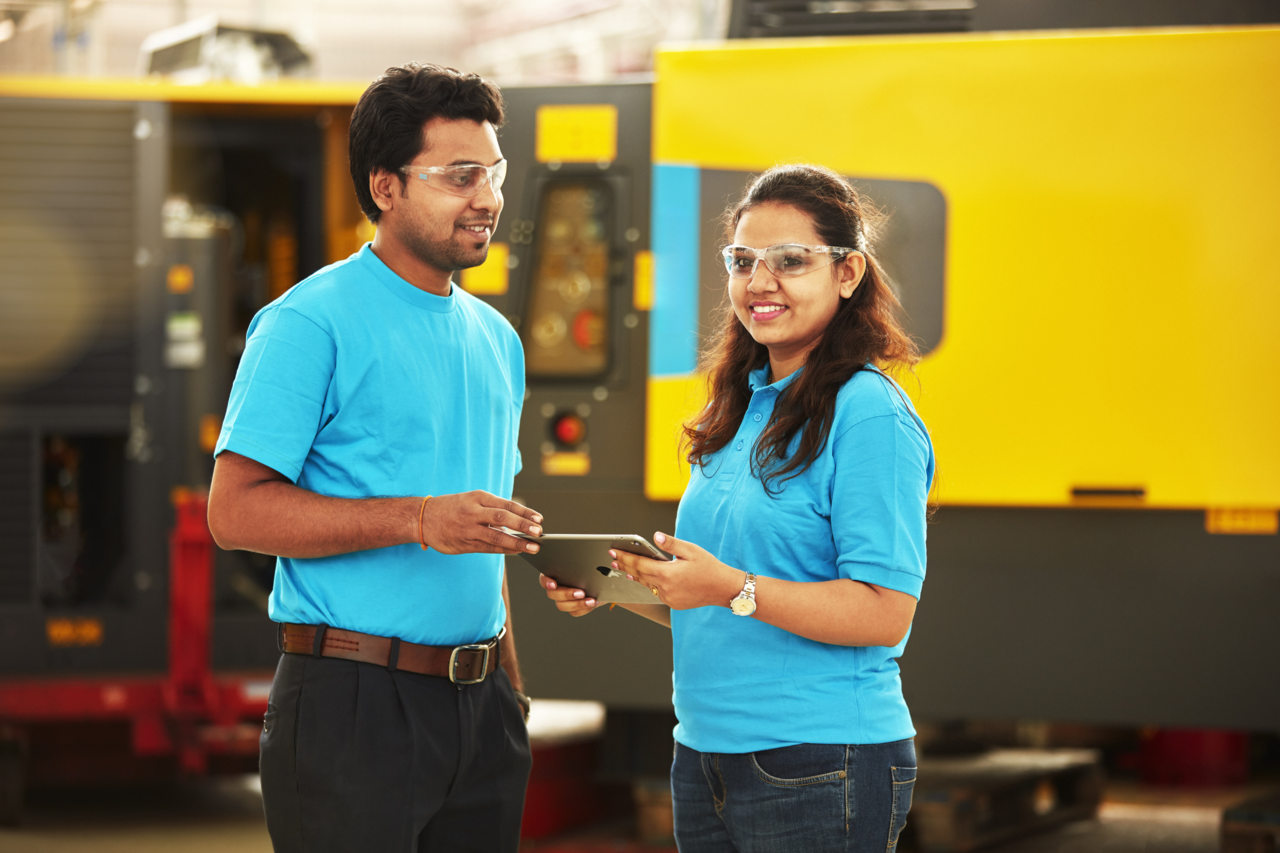 two technicians in light blue polo shirts and protective eye glasses in front of an industrial air compressor