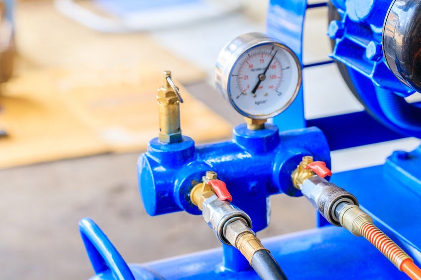 Image of a manifold with two piped threaded into it and a pressure gauge on top